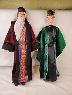 two dolls are posed next to each other on a white surface, one is wearing a green robe and the other has a red hat