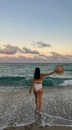 a woman standing in the ocean with a hat on her head and arms behind her back