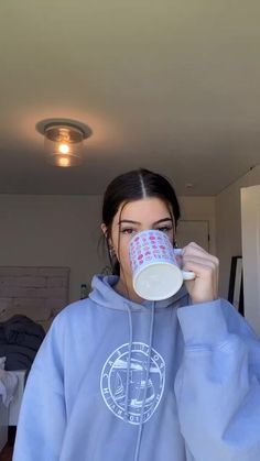 a woman in a blue sweatshirt drinking from a cup