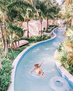 a woman in a hat is floating on an inner tube at the edge of a pool surrounded by palm trees