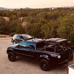 two pickup trucks parked next to each other in a parking lot with trees and mountains in the background