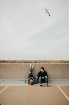 two people sitting on the ground with a bird flying overhead