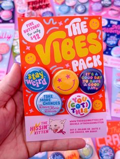 a hand holding up a pack of buttons in front of a pile of stickers