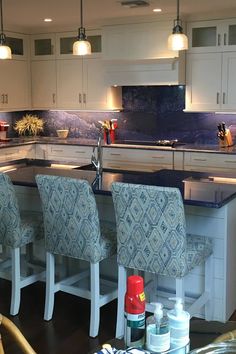 a kitchen with white cabinets and blue counter tops, along with bar stools in front of the island