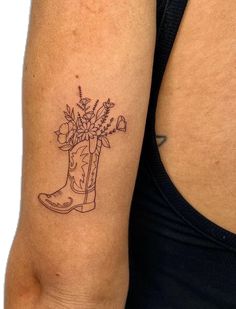 a woman with a tattoo on her arm holding a boot and flowers in the boot