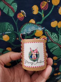 a hand holding a small christmas ornament in front of a wallpapered background