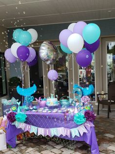 a purple and blue table topped with lots of balloons next to a brick floor covered in confetti