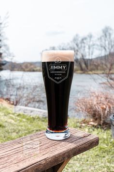 a glass of beer sitting on top of a wooden table next to a body of water