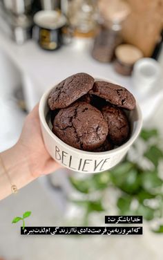 a hand holding a bowl filled with chocolate cookies