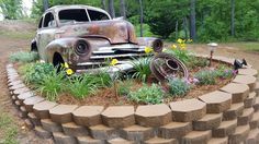 an old rusty car is sitting in the middle of a flower bed made out of bricks