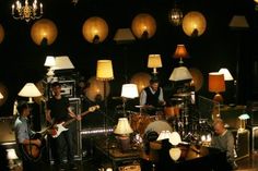 a group of people playing instruments in a room with lamps on the walls and floor