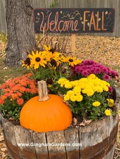 a wooden barrel filled with flowers next to a welcome fall sign