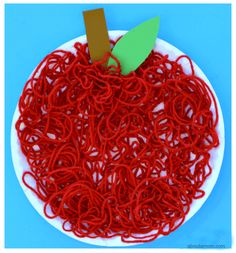 an apple made out of red noodles on a white plate with a green leaf sticking out of it