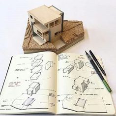 an open book with drawings on it and a house model sitting on top of it