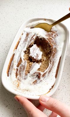 a person is holding a spoon over a dessert in a white dish with whipped cream on top