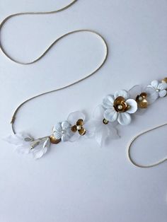 two necklaces with white flowers and gold accents on a white surface, one is being held by a string