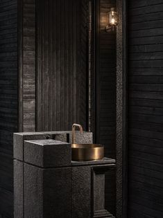 a bathroom sink sitting under a mirror next to a black wooden wall with a gold faucet