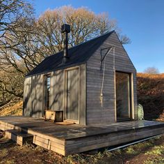 a small wooden building with a black roof and windows on the deck in front of some trees