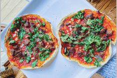 two pizzas with meat, cheese and spinach on them sitting on a white plate