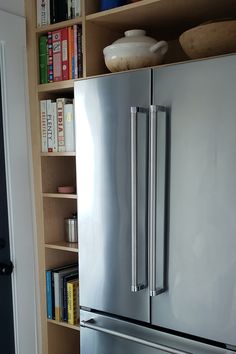 a stainless steel refrigerator in a kitchen next to bookshelves and a bookcase