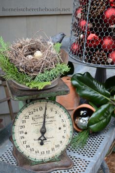 an old fashioned clock is sitting on a table next to some plants and other decorations