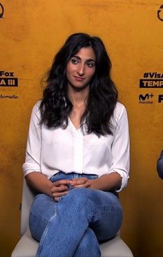 a woman sitting on top of a white toilet in front of a yellow wall and smiling