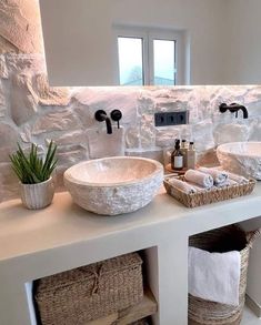 a bathroom with two sinks and baskets on the counter top next to each other in front of a stone wall