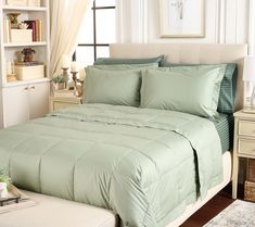 a bed with green comforter and pillows in a bedroom next to a white dresser