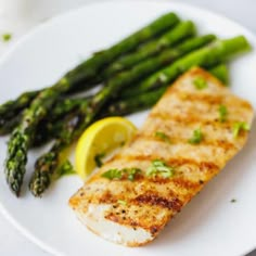 a white plate topped with fish and asparagus next to a lemon wedge on a table