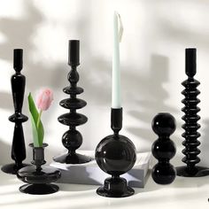 black candlesticks and vases are arranged on a white surface