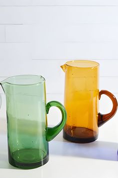 three different colored glass pitchers sitting next to each other on a white counter top,