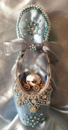 a blue vase with pearls, beads and a ring on it's side sitting on a satin surface