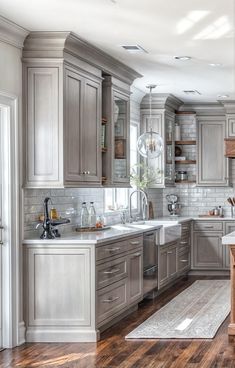 a large kitchen with wooden floors and gray cabinets in the center, along with white counter tops