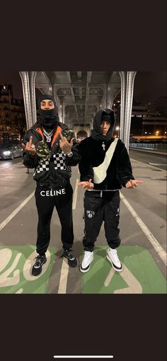 two young men standing next to each other in the middle of a parking lot at night