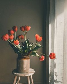 an arrangement of flowers in a vase sitting on a stool next to a window sill