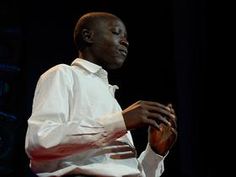 a man in white shirt and black pants sitting on stage with his hands folded out