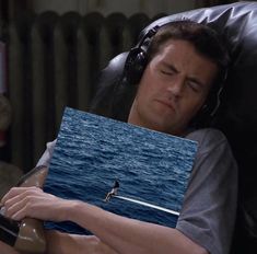 a man laying on top of a chair next to the ocean with his eyes closed