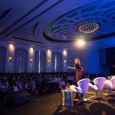 a woman standing on top of a stage in front of a crowd at a conference