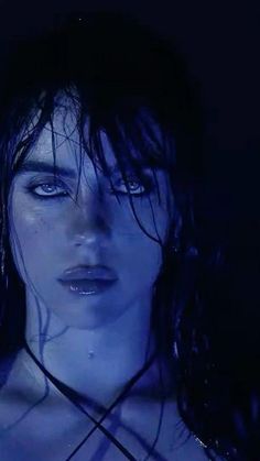 a woman with wet hair and blue eyes is posing for a photo in the dark