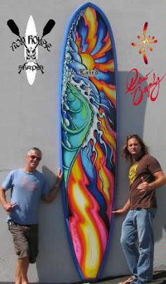 two men standing next to a surfboard on the side of a building with graffiti