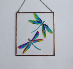 a glass panel with three dragonflies hanging from it's side on a chain