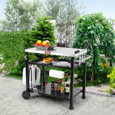 an outdoor kitchen cart with food and utensils on it in the middle of a garden