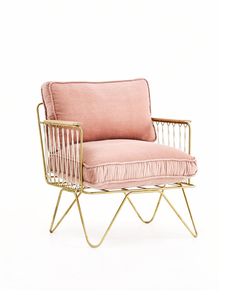 a pink chair with gold legs and a pillow on it's back, sitting in front of a white background