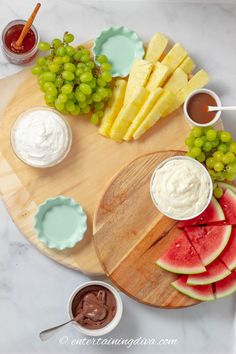 a wooden platter topped with watermelon slices, grapes and other fruit next to dips