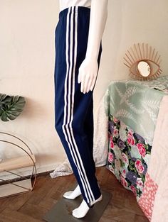 Beautiful Vintage Adidas stirrup track pants from the 1980s. Classic navy blue color with white stripes on the sides. Elasticated waistband. Permanent creases on the front. One zipped front pocket. Zipped leg openings.  For an amazing true Vintage street vibe wear with a simple tee and sneakers (or high heels)! BRAND: Adidas ERA: 1980s COLOUR: Navy blue, white FABRIC: 52% cotton, 48% nylon SIZE: Vintage size D 8, FR 183, IT 8, fits best modern size S to small M - please check the measurements be Stretch Pants With Side Stripes For Jogging, Stretch Joggers With Three Stripes For Jogging, Sporty Navy Pants With Three Stripes, Blue Sweatpants With Side Stripes For Jogging, Sporty Fitted Sweatpants With Three Stripes, Fitted Sporty Sweatpants With Three Stripes, Navy Sporty Pants With Three Stripes, Blue Sporty Bottoms With Contrast Stripes, 1980 Stirrup Pants