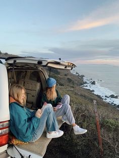 two people sitting in the back of a van on top of a hill near the ocean