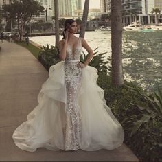 a woman in a wedding dress is standing on the sidewalk near some water and palm trees