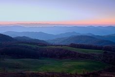 the mountains are covered with green grass and trees at sunset in the foreground is an empty field