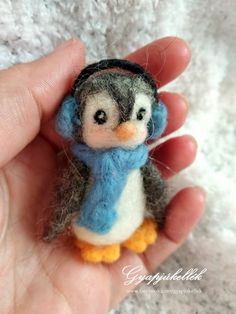 a small stuffed penguin wearing a blue scarf and headband is held in someone's hand