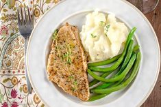 a white plate topped with meat, mashed potatoes and green beans next to a fork